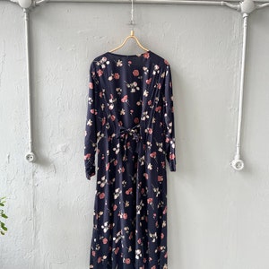K&ouml;nnte beinhalten: Ein lang&auml;rmeliges schwarzes Maxikleid mit einem Blumendruck mit rosa und wei&szlig;en Rosen. Das Kleid hat eine Schleife am R&uuml;cken.