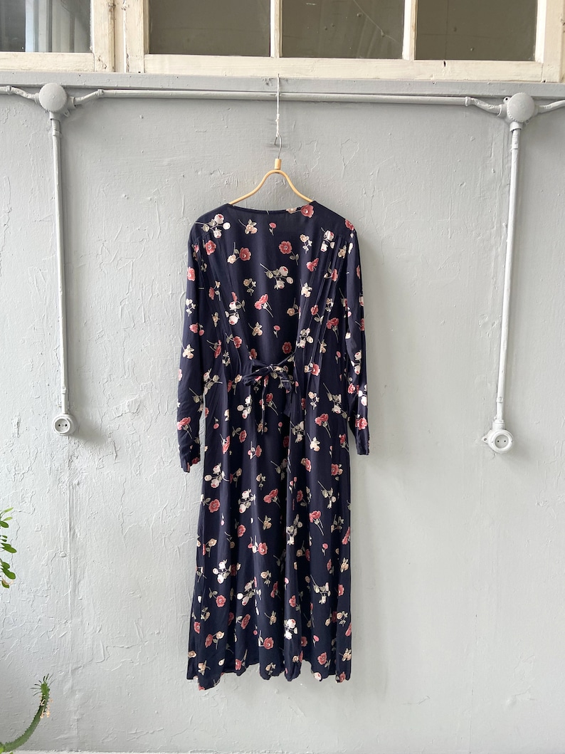 K&ouml;nnte beinhalten: Ein lang&auml;rmeliges schwarzes Maxikleid mit einem Blumendruck mit rosa und wei&szlig;en Rosen. Das Kleid hat eine Schleife am R&uuml;cken.