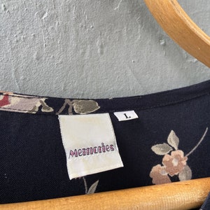 K&ouml;nnte beinhalten: Ein schwarzes Kleid mit floralem Muster und einem wei&szlig;en Etikett mit der Aufschrift "Memories" und einem Gr&ouml;&szlig;enetikett "L".
