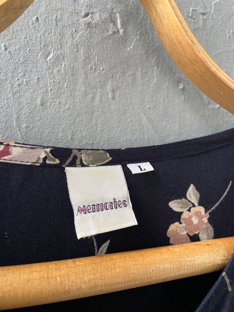 K&ouml;nnte beinhalten: Ein schwarzes Kleid mit floralem Muster und einem wei&szlig;en Etikett mit der Aufschrift "Memories" und einem Gr&ouml;&szlig;enetikett "L".