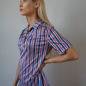 May include: A striped, short-sleeved shirt with red, blue, and white stripes. The shirt has a collared neckline and a button-up front.