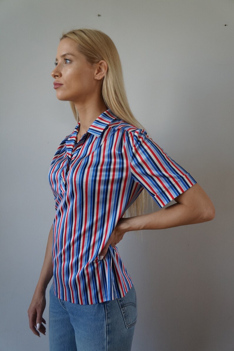 May include: A striped, short-sleeved shirt with red, blue, and white stripes. The shirt has a collared neckline and a button-up front.
