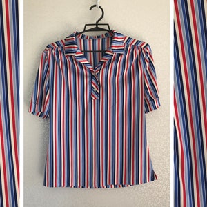 May include: A striped short-sleeved blouse with a collared neckline. The blouse has vertical stripes in red, blue, white, and light blue.
