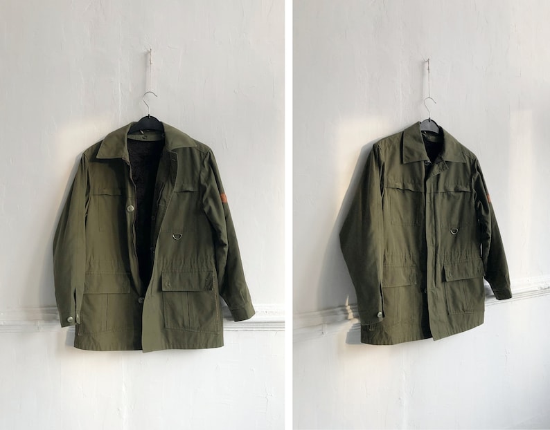 May include: A green utility jacket with a brown patch on the sleeve. The jacket has a button closure and two large pockets.