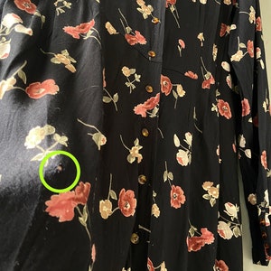 K&ouml;nnte beinhalten: Ein schwarzes, lang&auml;rmliges Kleid mit einem Blumendruck in Rosa- und Wei&szlig;t&ouml;nen. Das Kleid hat einen Knopfleisten vorne und einen gerafften Rock.