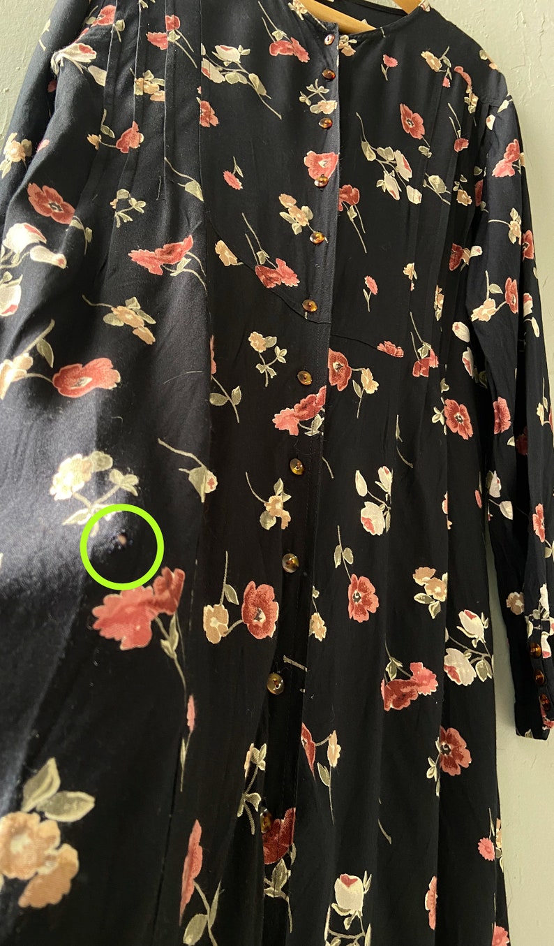 K&ouml;nnte beinhalten: Ein schwarzes, lang&auml;rmliges Kleid mit einem Blumendruck in Rosa- und Wei&szlig;t&ouml;nen. Das Kleid hat einen Knopfleisten vorne und einen gerafften Rock.