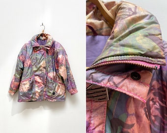 Könnte beinhalten: Eine mehrfarbige, floral gemusterte Steppjacke mit Reißverschluss. Die Jacke hat eine rosa, grüne und violette Farbgebung.