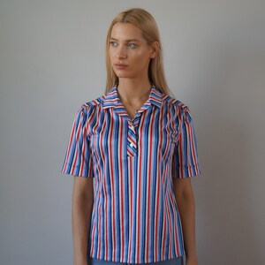 May include: A striped short-sleeved shirt with red, blue, and white stripes. The shirt has a collared neckline and a button closure.