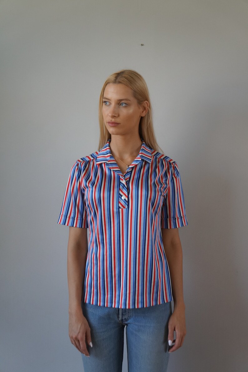 May include: A striped short-sleeved shirt with red, blue, and white stripes. The shirt has a collared neckline and a button closure.