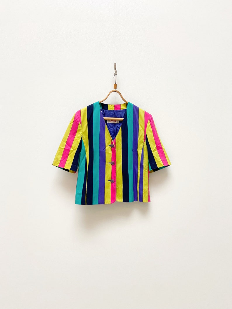 May include: A striped short-sleeved blazer with yellow, pink, purple, blue and black stripes. The blazer has a button closure and a v-neck.