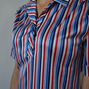 May include: A short-sleeved, collared shirt with red, blue, and white diagonal stripes. The shirt has a button closure and a relaxed fit.