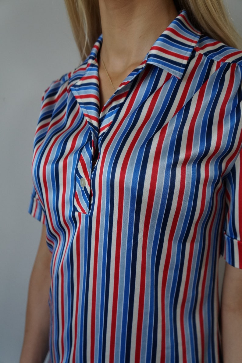 May include: A short-sleeved, collared shirt with red, blue, and white diagonal stripes. The shirt has a button closure and a relaxed fit.