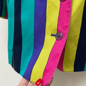 May include: A striped blazer with a yellow, pink, green, purple, and navy blue pattern. The blazer has two buttons on the front.