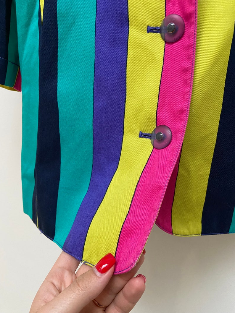 May include: A striped blazer with a yellow, pink, green, purple, and navy blue pattern. The blazer has two buttons on the front.