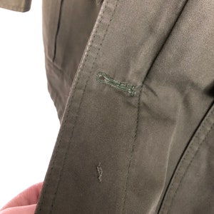May include: Close-up of a dark green jacket with a button closure. The button is made of metal and has a loop design.