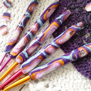 May include: Set of five colorful crochet hooks with a purple, orange, and white marbled design. The hooks are numbered 8, 9, 10, 11, and 12.