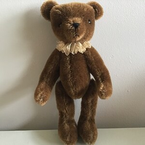 May include: A brown teddy bear with a beige lace collar. The bear has black eyes and a black nose.