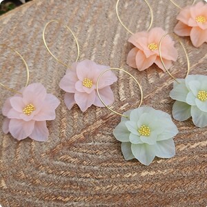 以下が含まれることがあります： パステルカラーの繊細な花柄フープイヤリングのセット。イヤリングは、薄いピンクと薄い緑の花のデザインで、ゴールドのアクセントが施されています。