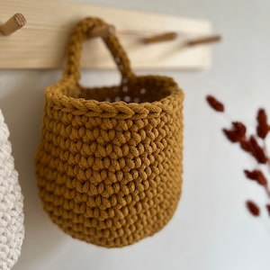 Pu&ograve; includere: Un cesto appeso in crochet di colore giallo senape con un manico in corda.