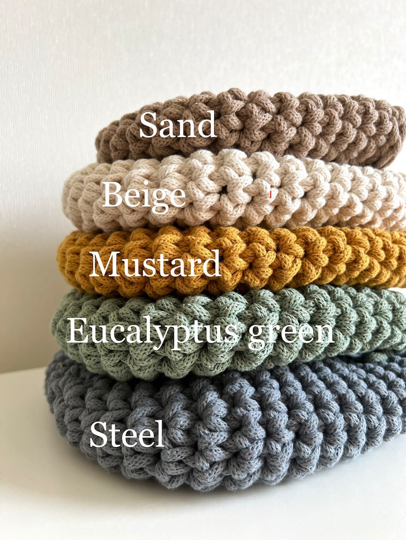 Pu&ograve; includere: Cinque sottobicchieri rotondi all'uncinetto in diversi colori, impilati uno sopra l'altro. I colori sono sabbia, beige, senape, verde eucalipto e acciaio.