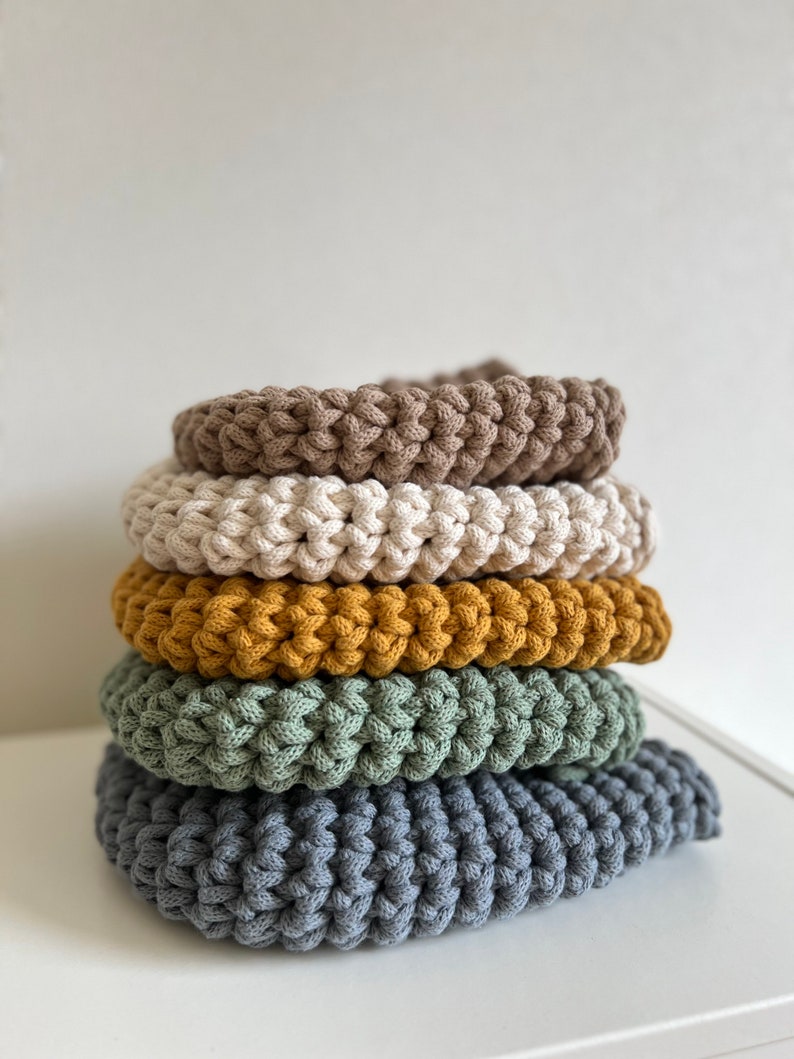 Pu&ograve; includere: Un mucchio di cinque cuscini rotondi all'uncinetto in vari colori, tra cui marrone, beige, giallo senape, verde e grigio.