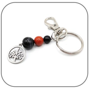 May include: A silver key chain with a tree of life charm and three beads: black, red, and black.