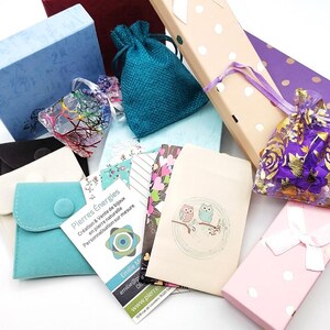 K&ouml;nnte beinhalten: Eine Auswahl an kleinen Geschenkboxen und Beuteln in verschiedenen Farben und Mustern, darunter Blau, Lila, Rosa und Braun. Einige Boxen haben Punkte, w&auml;hrend andere Blumenmuster haben. Die Boxen sind mit kleinen Gegenst&auml;nden gef&uuml;llt, wie z. B. Schmuck, Kristallen und anderen Kleinigkeiten. Der Text auf einer der Karten lautet "Pierres Energies Creation & Vente de bijoux en pierre naturelle Personnalisation sur mesure Emille M emiliep 06 www.pierre"