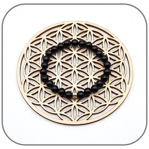 May include: Black beaded bracelet with a gold charm on a wooden background.