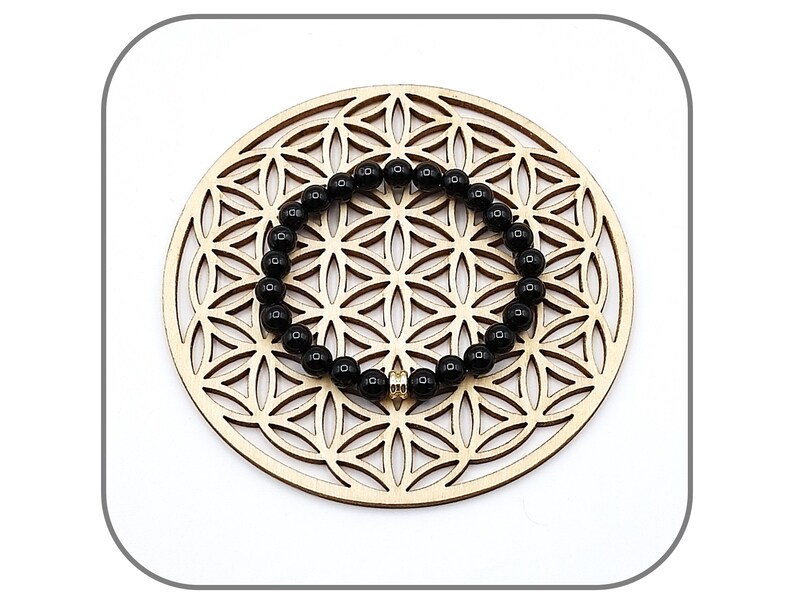 May include: Black beaded bracelet with a gold charm on a wooden background.