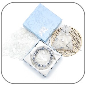 May include: A blue gift box with a white and gray crystal bracelet inside. The bracelet is made of round, gray and white stones. The box is surrounded by loose white crystals.