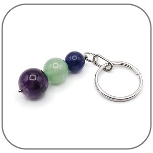Peut inclure: Un porte-clés argenté avec trois perles rondes en pierres précieuses. Les perles sont violettes, vertes et bleues.