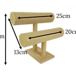 May include: A beige fabric-covered jewelry display stand. The stand has two horizontal bars, 9.8 inches and 7.9 inches long, supported by vertical posts. The base is 5.1 inches wide, and the total height is 7.5 inches. Ideal for bracelets and bangles.