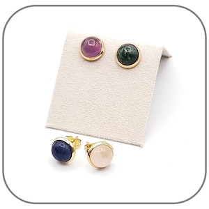 Op de afbeelding: Vier paar gouden oorbelletjes met verschillende gekleurde edelstenen. De oorbelletjes hebben een ronde, cabochon geslepen edelsteen die in een gouden zetting is gezet. De edelstenen zijn roze, groen, blauw en lichtroze.