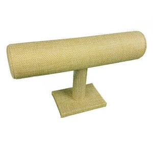 May include: A beige fabric-covered jewelry display stand. The stand has a rectangular base, a vertical support, and a horizontal, cylindrical bar for displaying bracelets or bangles. The fabric has a woven texture.