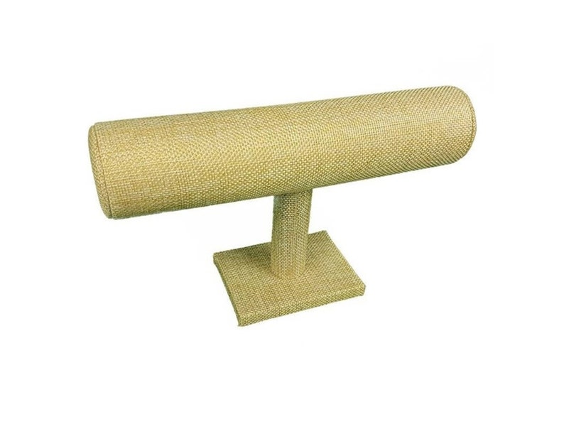 May include: A beige fabric-covered jewelry display stand. The stand has a rectangular base, a vertical support, and a horizontal, cylindrical bar for displaying bracelets or bangles. The fabric has a woven texture.