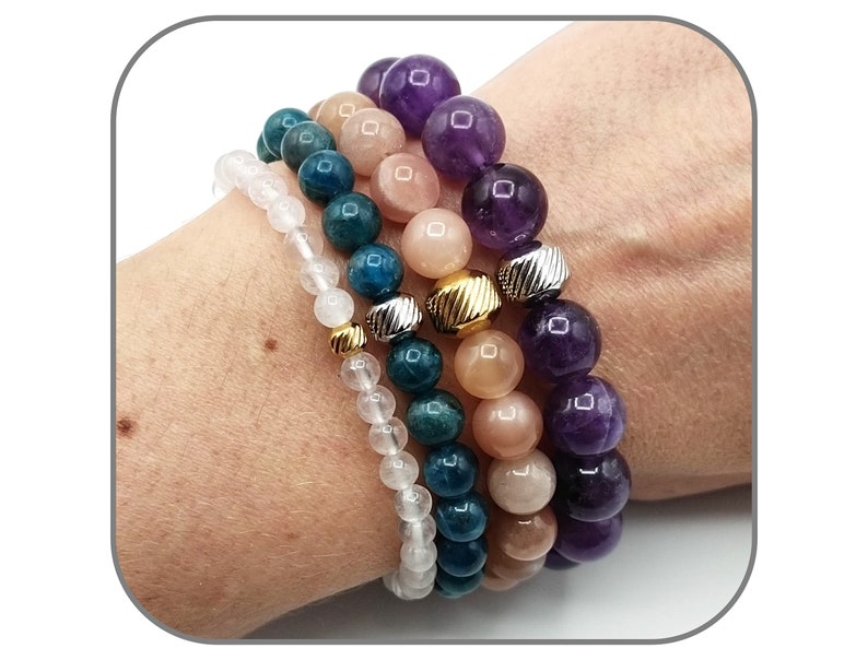 May include: Four stacked bracelets with different colored beads. The top bracelet has purple amethyst beads, the second bracelet has peach sunstone beads, the third bracelet has teal apatite beads, and the bottom bracelet has white quartz beads.