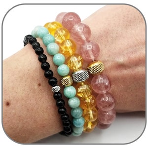 May include: Four stacked bracelets with different colored beads. The top bracelet is pink, the second is yellow, the third is light blue, and the bottom is black.