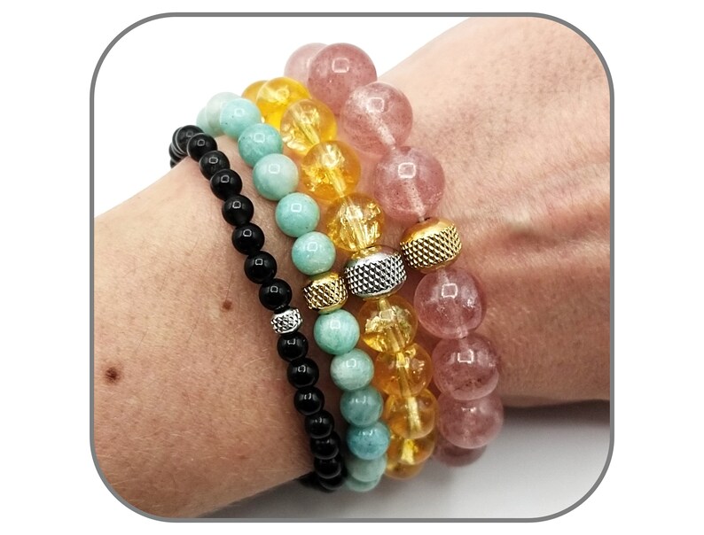 May include: Four stacked bracelets with different colored beads. The top bracelet is pink, the second is yellow, the third is light blue, and the bottom is black.