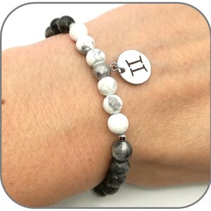 K&ouml;nnte beinhalten: Ein Armband aus schwarzen und wei&szlig;en Perlen mit einem silbernen Anh&auml;nger, auf dem "II" steht.