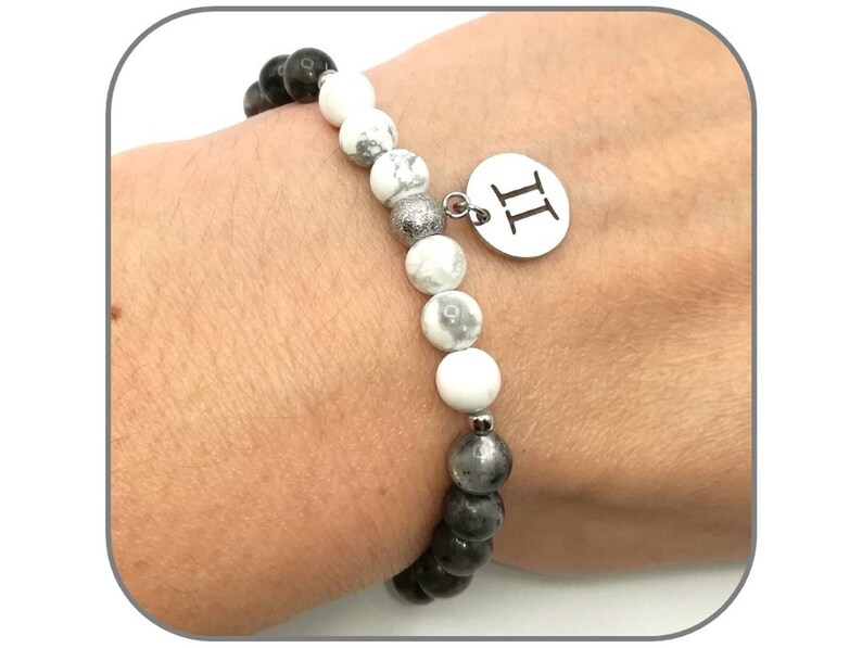 K&ouml;nnte beinhalten: Ein Armband aus schwarzen und wei&szlig;en Perlen mit einem silbernen Anh&auml;nger, auf dem "II" steht.