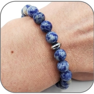 May include: A blue and white gemstone bracelet with a silver bead accent. The bracelet is made of round beads and is worn on a person's wrist.