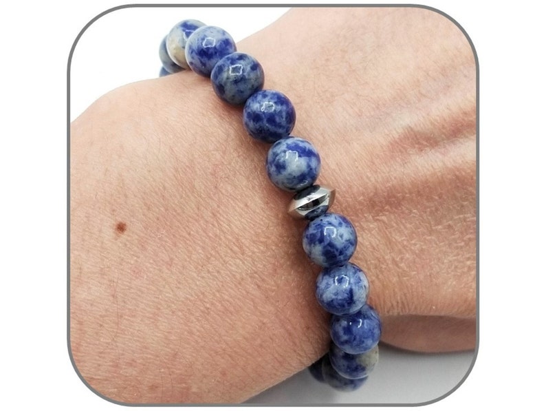 May include: A blue and white gemstone bracelet with a silver bead accent. The bracelet is made of round beads and is worn on a person's wrist.