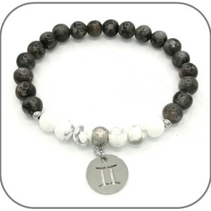 K&ouml;nnte beinhalten: Ein Armband aus schwarzen und wei&szlig;en Perlen mit einem silbernen Anh&auml;nger mit dem Zwillings-Sternzeichen. Das Armband hat eine silberne Zwischenperle und einen silbernen Verschluss.