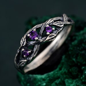May include: A silver ring featuring a twisted branch design with three purple amethyst gemstones.