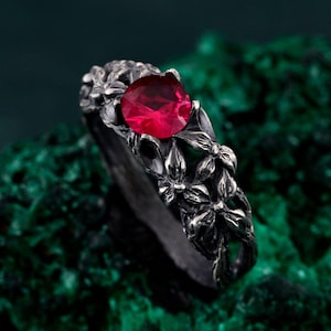 May include: A silver ring with a red gemstone set in a floral design.