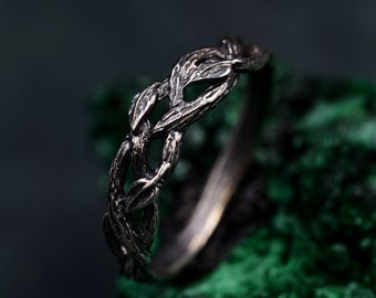 May include: A dark oxidized silver ring featuring a textured, intertwined vine and leaf design. The band has a rustic, organic appearance with deep crevices and raised details that mimic the natural structure of twisted branches and foliage.