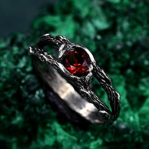 Könnte beinhalten: Ein silberner Ring mit einem roten Edelstein, der in einem astförmigen Design gefasst ist.