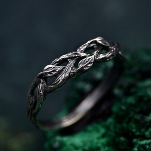 May include: A silver ring with a design of intertwined branches and leaves. The ring is made of metal and has a rustic, organic look.