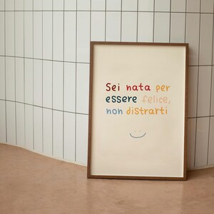 May include: A framed print with the text "Sei nata per essere felice, non distrarti" in colorful lettering. A simple smiley face is drawn below the text.