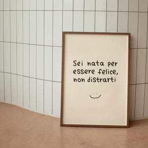 May include: A framed print with a light beige background and a dark brown wooden frame. The print features black text that reads "Sei nata per essere felice, non distrarti" and a small smiley face.